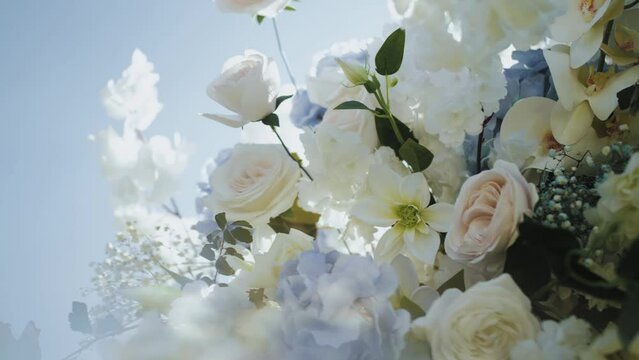  Close-up of wedding arch decorated with flowers in white and blue colors, roses, chrysanthemums and hydrangeas, blue sky on the background slow motion, outside wedding ceremony.
