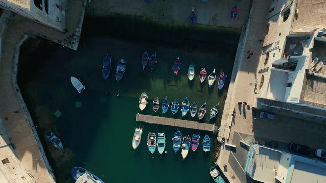 Top down drone lowering shots of traditional fishing boats moored in the Italian city of Monopoli on a sunny day.