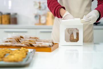 Asian woman bakery shop owner preparing customer order cookie in delivery box on kitchen counter....