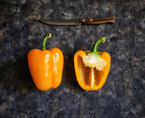 Top view on yellow bell peppers and knife with wooden handle on rustic black concrete table. Horizontal website banner with orange paprika.