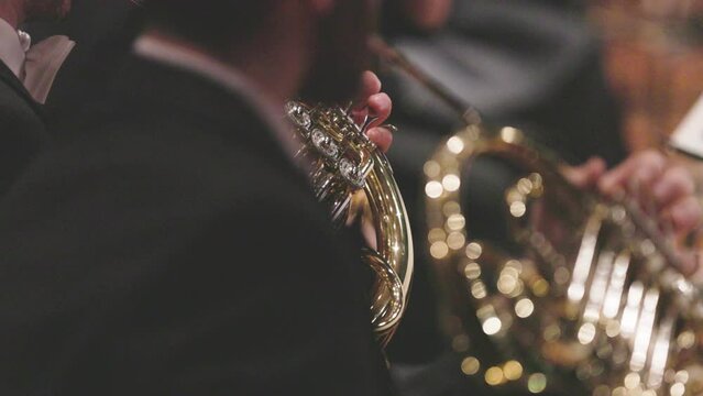 A musician playing a shiny French horn during a symphony orchestra concert