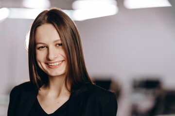 Smiling businesswoman on blurred background. Indoor shot of successful young woman. Happy female office worker looking at camera