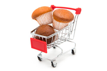 Freshly baked muffins in supermarket shopping cart isolated on white background. Food delivery...