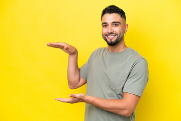 Young Arab handsome man isolated on yellow background holding copyspace to insert an ad