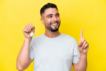 Young Arab man holding home keys isolated on yellow background intending to realizes the solution...