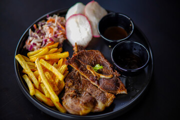 Close-up premium quality Pork Chop Steak Black Pepper with woman hand eating and black pepper sauce in black cups, French fries, Vegetables salad, in black background