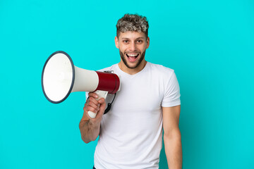 Young handsome caucasian man isolated on blue background holding a megaphone and with surprise...