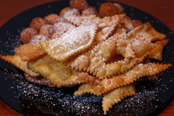 Frappe or chiacchiere and onbaked castagnole typical Italian carnival fritters dusted with powdered sugar. Biscuits with sugar for the carnival of Venice. Traditional sweet pastries
