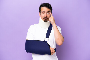 Young caucasian man wearing a sling and neck brace isolated on purple background thinking an idea