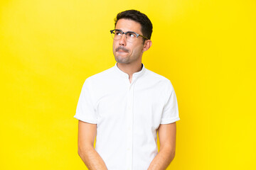 Young handsome man over isolated yellow background having doubts while looking up