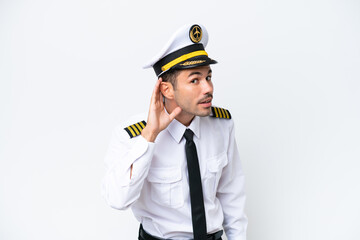 Airplane pilot over isolated white background listening to something by putting hand on the ear