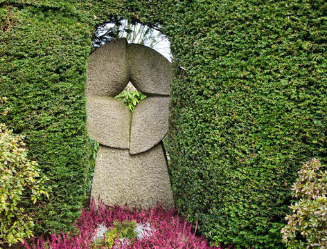 gro&szlig;er Grabstein inmitten eines gr&uuml;nen Strauches und davor bl&uuml;hende Eriken auf einem Friedhof in Velbert