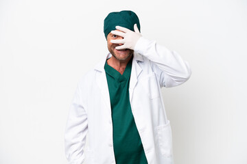 Middle age surgeon in green uniform isolated on white background covering eyes by hands and smiling