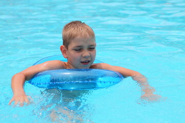 A cheerful child in a blue swimming circle in a pool with clear blue water. Holidays on the sea.