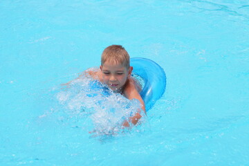 Fototapeta na wymiar Funny little boy swims in a pool in an blue life preserver