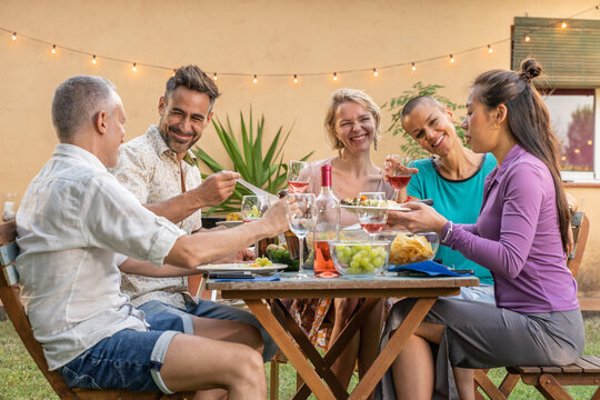 Multicultural friends eating and drinking happy smiling and laughing in the patio. Middle-aged cheerful people around the table. High quality photo