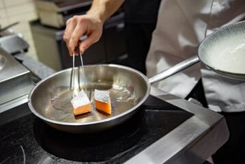 man chef cooking fried salmon fish in frying pan on kitchen