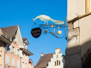 Biel, Switzerland - April 16th 2023: Restaurant signpost with a peafowl in front of historic buildings