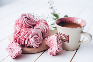 Raspberry marshmallows on a wooden stand. Homemade marshmallows with a hot cup of coffee on a white background. Pink marshmallows and a pink cup. Coffee in a pink cup. Cooking. Desserts and drinks. 