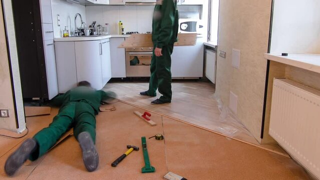Carpenter workers in green uniform installing wood parquet board on kitchen during flooring work timelapse