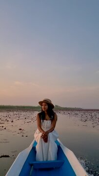 Sunrise at The sea of red lotus, Lake Nong Harn, Udon Thani, Thailand. An Asian woman in a wooden boat during sunrise at the red lotus lake in Thailand 