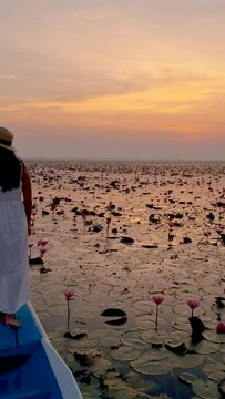 Asian women in a wooden boat during sunrise at the red lotus lake in Thailand , Sunrise at The sea of red lotus, Lake Nong Harn, Udon Thani, Thailand