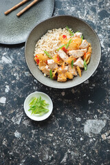 Bowl of korean chicken and kimchi stir-fry with brown rice, above view on a dark-brown granite background, vertical shot with space