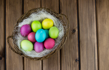 Obraz na płótnie Canvas Happy Easter concept. Top view of basket full of colorful painted eggs on wooden background