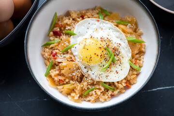 Bowl of kimchi fried rice topped with chicken egg, horizontal shot on a black marble background, middle closeup