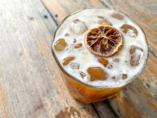 Iced coffee soda drink topped with dried lemon slices on wooden table.  Fresh cold drink during the day or summer. High angle.