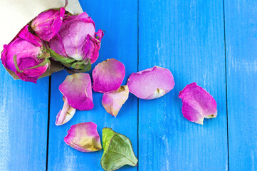 Top view of dried rose petals in old paper envelope on blue wooden background