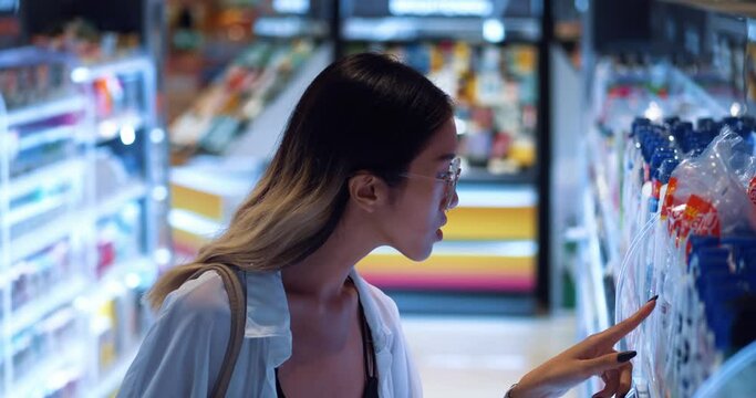 Young woman chooses shampoo in the body care section of supermarket. Pretty Asian female chooses beauty products for self-care in a supermarket. Attractive girl buys cosmetics and shampoos