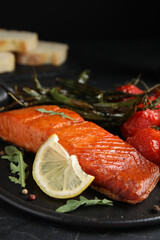 Delicious cooked salmon with lemon on black table, closeup. Healthy meals from air fryer