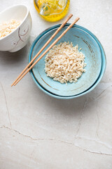 Turquoise bowls with brown rice on a beige stone background, vertical shot with copy space, top view
