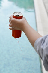 Woman holding tasty open canned beverage near swimming pool, closeup