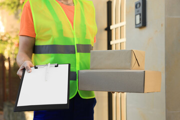 Courier in uniform holding order receipt and parcels outdoors closeup
