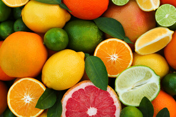 Different fresh citrus fruits and leaves as background, top view.