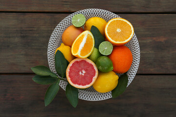 Bowl with different citrus fruits and leaves on wooden table, top view