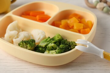 Baby food. Section plate with different vegetables on white wooden table, closeup
