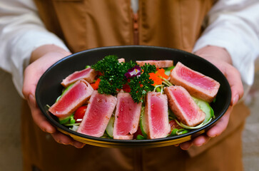 Fresh tuna salad served with sunflower sprouts and fresh organic lettuce in an elegant black plate placed on a wooden table and old newspapers.