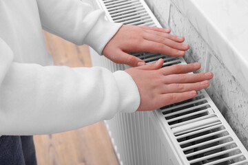 Naklejka premium Girl warming hands on heating radiator indoors, closeup