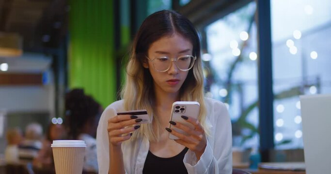 Asian lady credit card holder use mobile phone pay online buy consumer goods order services on ecommerce websites from cafe. Female make safe transaction with credit card and mobile phone at ebank app