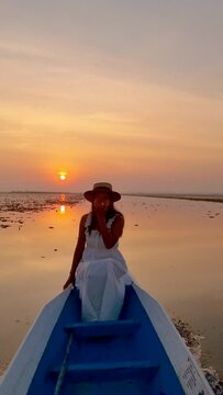 Sunrise at The sea of red lotus, Lake Nong Harn, Udon Thani, Thailand. An Asian woman in a wooden boat during sunrise at the red lotus lake in Thailand Isaan region
