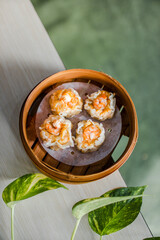 Top view of steamed prawn dimsum in bamboo steamer on wooden table with leaves as decoration