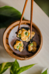 Close up of steamed dimsum in bamboo steamer on wooden table with chopsticks and leaves as...