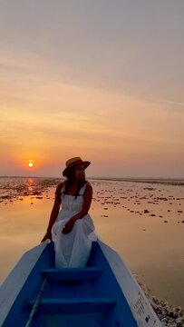 Sunrise at The sea of red lotus, Lake Nong Harn, Udon Thani, Thailand. A Asian women in a wooden boat during sunrise at the red lotus lake in Thailand 