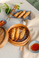 Fried tempura prawn Dimsum in traditional bamboo basket with 
tomato sauce, slice of chili on bowl and chopsticks on wooden background