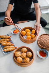 Close up female hand taking fried dimsum with chopsticks in traditional bamboo bowl on wooden table background
