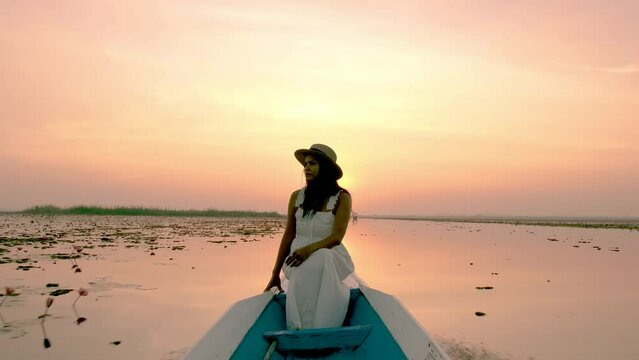 Sunrise at The sea of red lotus, Lake Nong Harn, Udon Thani, Thailand. A Asian women in a wooden boat during sunrise at the red lotus lake in Thailand 