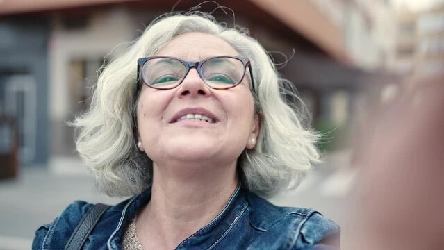 Middle age woman with grey hair smiling confident having video call at street